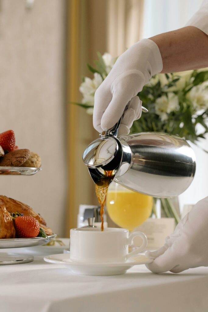 Elegant morning setup with coffee and pastries served by a gloved hand, showcasing luxury room service.